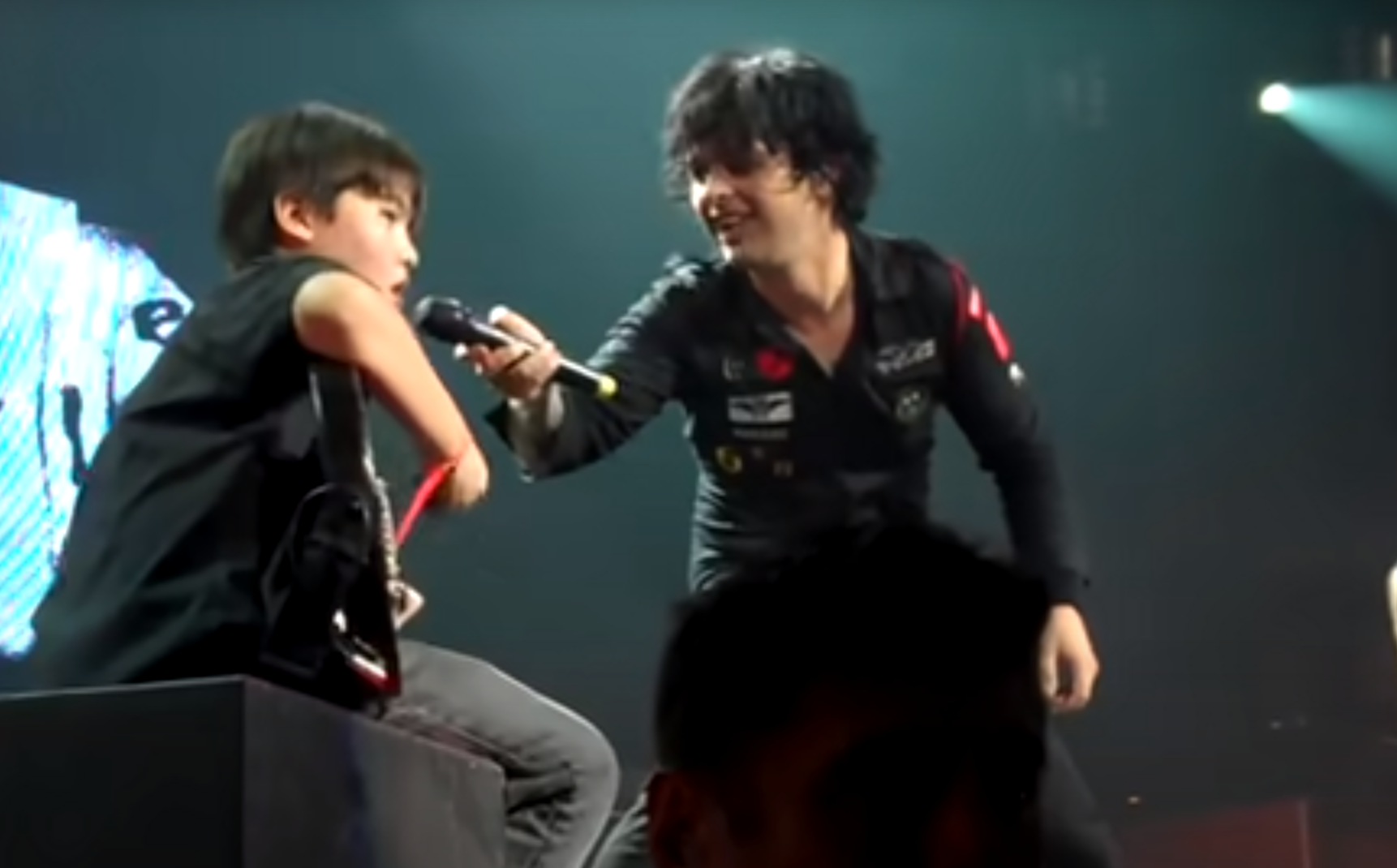 A young fan on a Green Day live stage plays guitar and sing with Billie Joe Armstrong